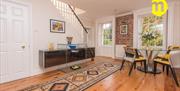 Image shows lounge area with wooden floor, decorative runner carpet, table and chairs, Staircase leading to upstairs.