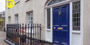 Image shows royal blue front door with iron railing to the left of the door Door leads out onto footpath on street