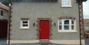 Image shows red front door of stone property with gravel drive