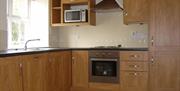 A kitchen with wooden cabinets, a sink, microwave and hob/oven.