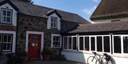 Image is of side view of property with red door with glass and bicycle leaning againt a row of windows.