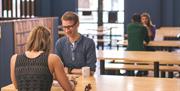 A photo of couples sitting at benches in a communal dining area.