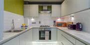 A tiled kitchen with lights, a sink, oven and other kitchen equipment.