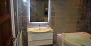The bathroom with large corner bath, sink, mirror and patterned wall tiles