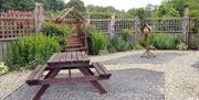 Image shows wooden picnic bench in gravel courtyard setting