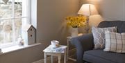 Image shows lounge area with sofa, table with cup of tea and magazine