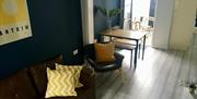 An open plan living room with a sofa, chair, kitchen bench and a back door leading to a small outdoor patio.