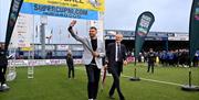 two men walk on to a football pitch under a branded 'SuperCupNI' arch