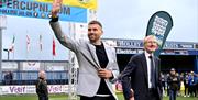 two men walk on to a football pitch under a branded 'SuperCupNI' arch while waving