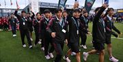 a team wearing black athletic uniforms walk on to a football pitch as part of a parade procession