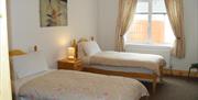 Image shows twin bedroom with beside table and lamp between the beds