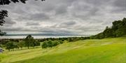 The green with woodland and coast in background