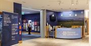 Reception area of the Discover Ulster-Scots Centre with informational displays and a circular front desk. A member of the public is viewing an exhibit