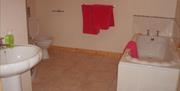 A tiled bathroom with a sink, toilet, bathtub and red towels.