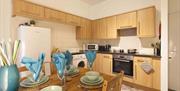 A fully fitted kitchen with wooden cupboards and a fully set table with wine glasses and crockery.