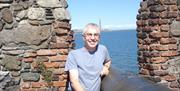 A smiling man standing next to a wall on the coast.