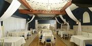 A ballroom filled with tables, decorative hanging curtains and lights.