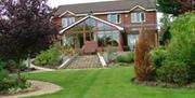 A large B&B on a lawn with trees and stone stairs leading to a large conservatory.