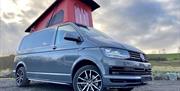 Image of a grey Volkswagen campervan with a red pop-top roof.