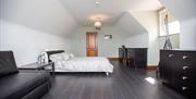 Image shows double bedroom with sofa, desk and chair. Dark wooden floor.