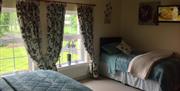 An upstairs bedroom with two beds, a TV and two windows with a view of the lawn.