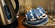 Image shows tray with saucers and cups next to a kettle