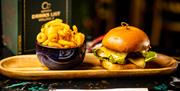 A wooden tray with a bowl of curly fries and a cheeseburger.