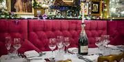 A table with red felt booth seating set with wine glasses and a champagne bottle holding a candle.