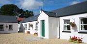 Image shows front of whitewashed property with green door and gravel drive. Flowerbeds on gravel outside windows