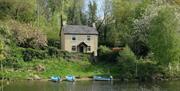 A house in a wooded area with a river and boats outside.