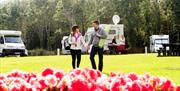 Image shows couple walking hand in hand on the grass with caravans in the background