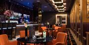 A bartender making drinks in a bar with tables & chairs and booths.