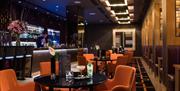 A bartender making drinks in a bar with tables & chairs and booths.