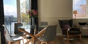 Glass dining room table with chairs, flowers and a balcony with views of the river.