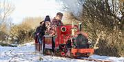 a photo of a group of adults on a small train surrounded by snow and trees