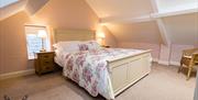 Image shows double bedroom with bedside tables and lamps and wicker chair