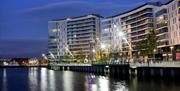 A curving apartment building at night on a seaside walkway.