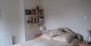 A double bed with cream linen and two shelves filled with books