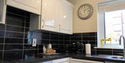 A black tiled kitchen with white cupboards, a toaster, microwave, sink and a cake.