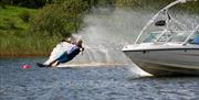 Image is of a male water-skier and boat beside them on the water