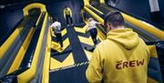 Image is of children climbing up a steep wall with a man with a Crew sweatshirt at the bottom