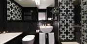 A black tiled bathroom with a bath, toilet, sink and walk-in shower.