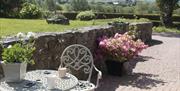 Image shows outside area with wrought iron table and chair, grassy area and view of the countryside beyond