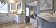 Image shows kitchen area with wooden floor, breakfast bar and 2 stools plus view into open plan lounge area