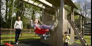 family playing on swings of wooden play climbing frame