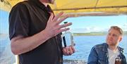 a person holding a bottle of gin speaks on a boat