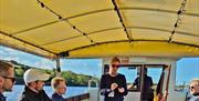 a group watches on as a tour guide talks to them onboard a river boat