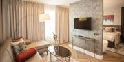 A photo of a hotel room with a thin wall separating a bedroom from a sitting area with a sofa and TV.