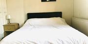 A double bedroom with white sheets, a bedside table with a lamp and a painting.