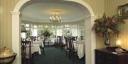 Archway leading to a conservatory dining room with tables and chairs.